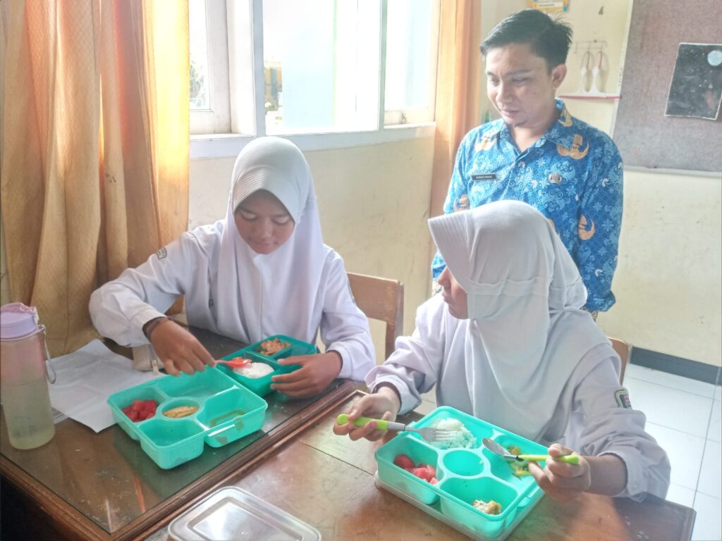 Ketfot: Seorang siswi kelas 9D SMPN 2 Ciamis, Gita Meikasari (kiri) memindahkan makanan dari program makan bergizi gratis untuk dimakan setelah waktu berbuka puasa